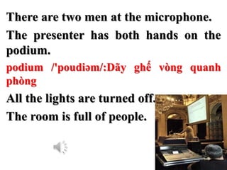 There are two men at the microphone.
The presenter has both hands on the
podium.
podium /'poudiəm/:Dãy ghế vòng quanh
phòn...