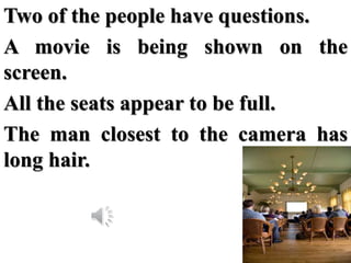 Two of the people have questions.
A movie is being shown on the
screen.
All the seats appear to be full.
The man closest t...