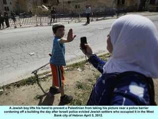 A Jewish boy lifts his hand to prevent a Palestinian from taking his picture near a police barrier
cordoning off a buildin...