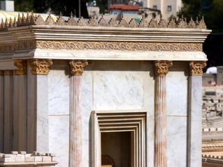 Desde el oeste vemos la parte superior de la fachada este del templo
“La vid de oro” decora la banda horizontal. En el borde superior de la
azotea, donde se alhojaban palomas y otros pájaros, está
ornamentado con “puntos de oro”.
Las dos columnas unidas a la fachada en ambos lados de la puerta
se llaman “Jachin y Boaz” (1Reyes 7, 21). Los capitales de las
columnas combinan los estilos corinto y jónico.
 