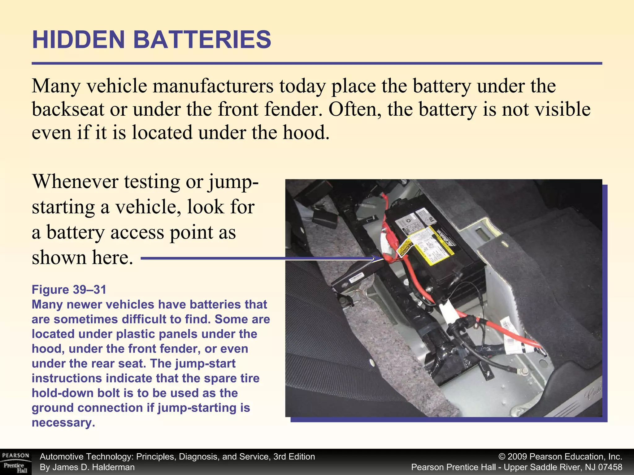 HIDDEN BATTERIES Many vehicle manufacturers today place the battery under the backseat or under the front fender. Often, the battery is not visible even if it is located under the hood.  Figure 39–31 Many newer vehicles have batteries that are sometimes difficult to find. Some are located under plastic panels under the hood, under the front fender, or even under the rear seat. The jump-start instructions indicate that the spare tire hold-down bolt is to be used as the ground connection if jump-starting is necessary. Whenever testing or jump-starting a vehicle, look for a battery access point as shown here. 