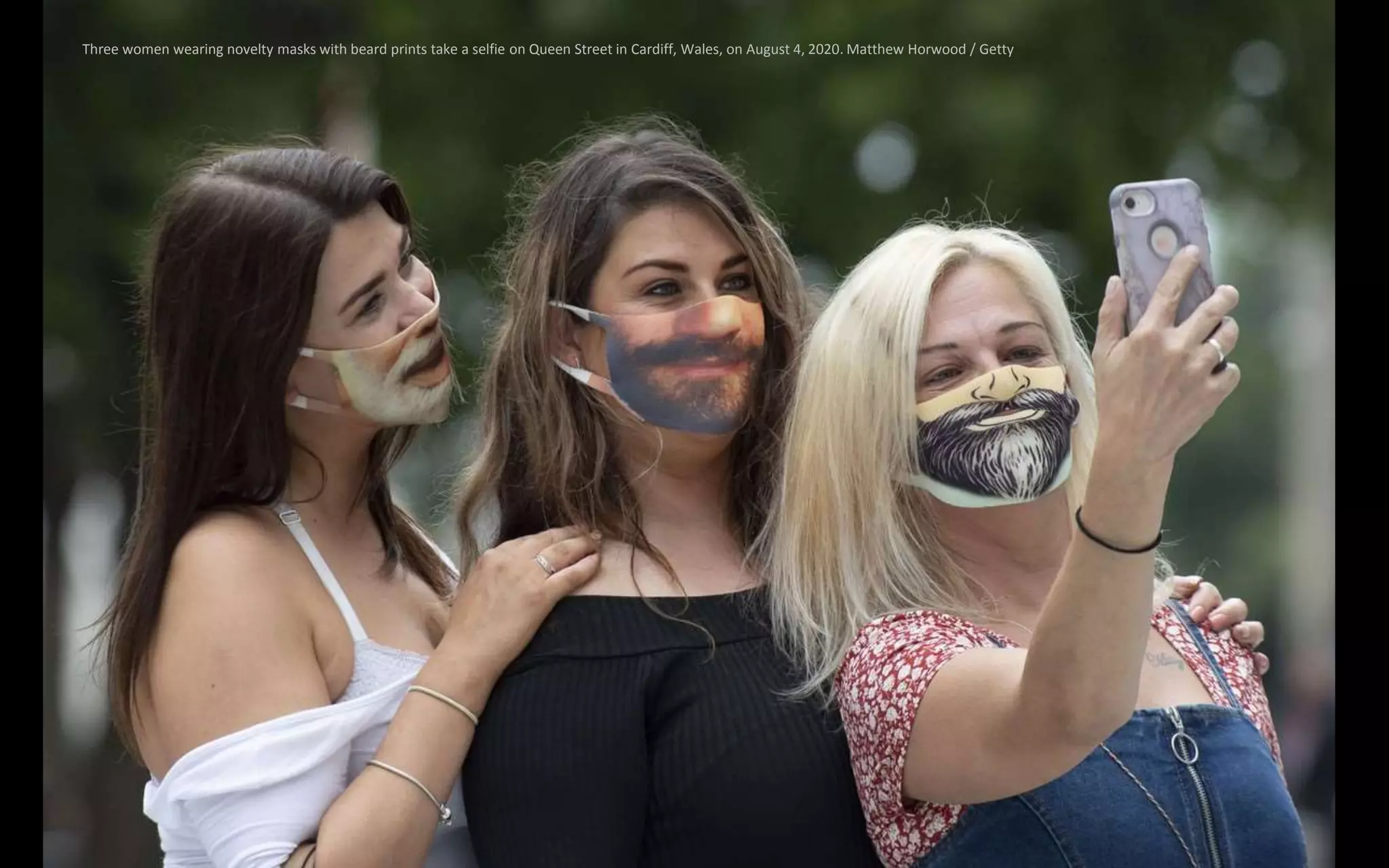 Three women wearing novelty masks with beard prints take a selfie on Queen Street in Cardiff, Wales, on August 4, 2020. Matthew Horwood / Getty
 