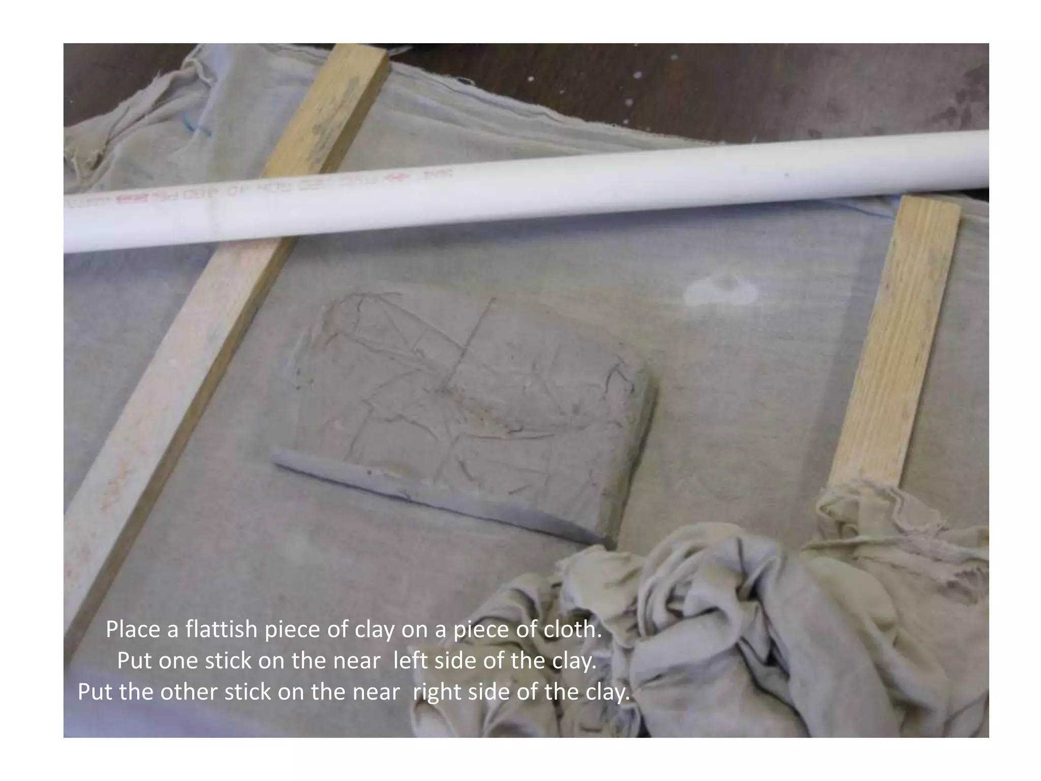 Place a flattish piece of clay on a piece of cloth. Put one stick on the near  left side of the clay.Put the other stick on the near  right side of the clay. 