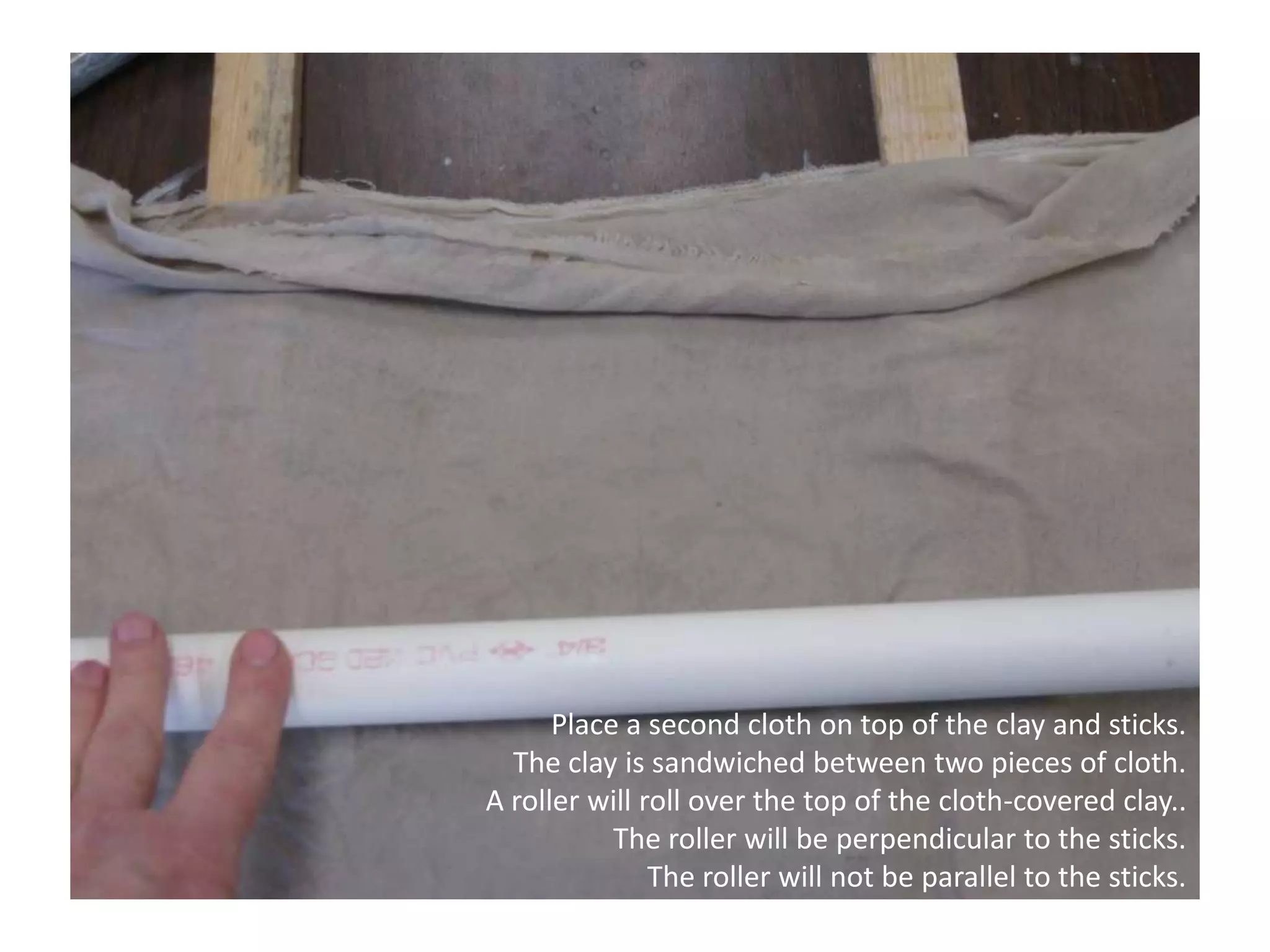 Place a second cloth on top of the clay and sticks. The clay is sandwiched between two pieces of cloth. A roller will roll over the top of the cloth-covered clay.. The roller will be perpendicular to the sticks.The roller will not be parallel to the sticks.
