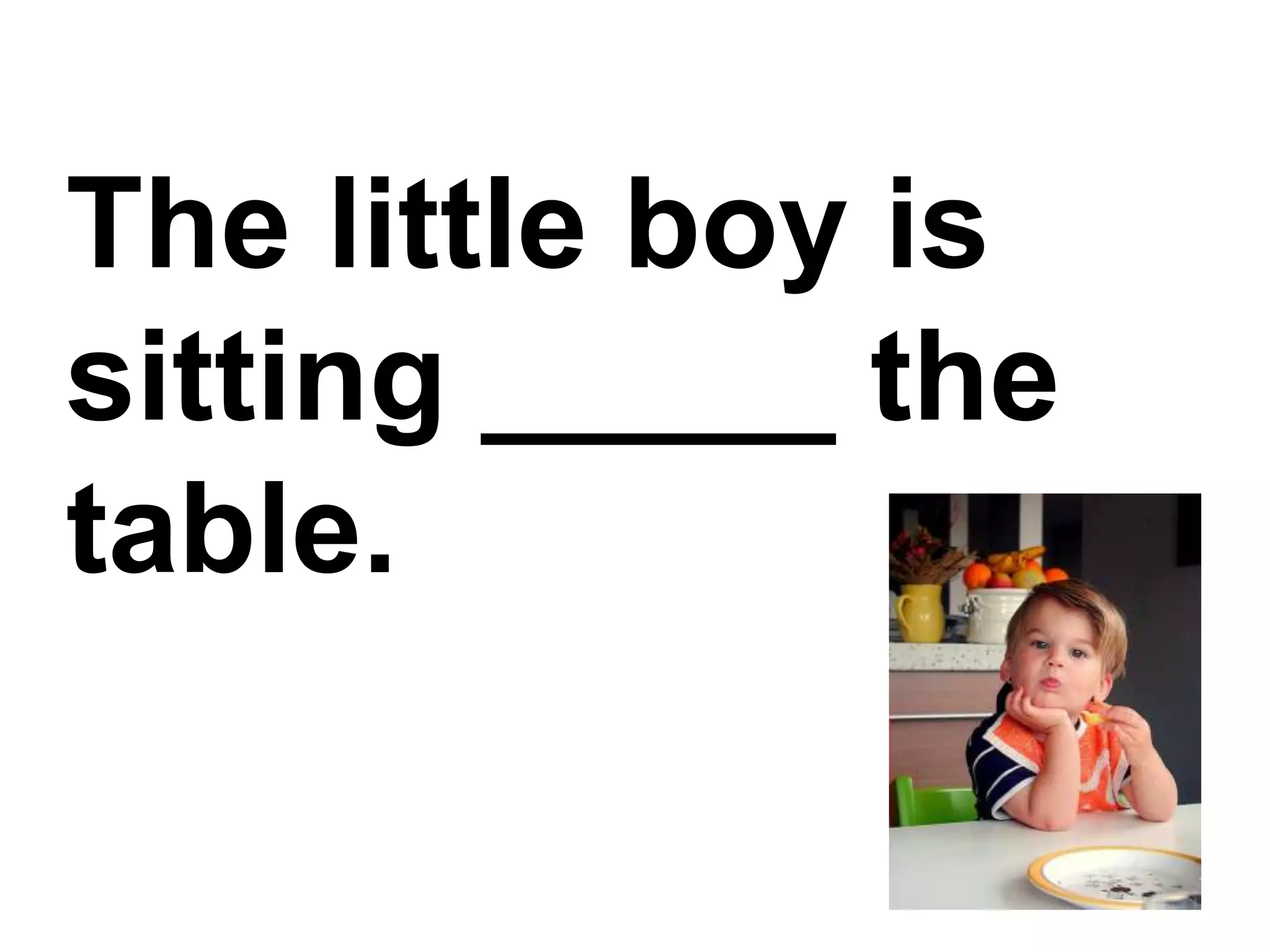 The little boy is sitting _____ the table.