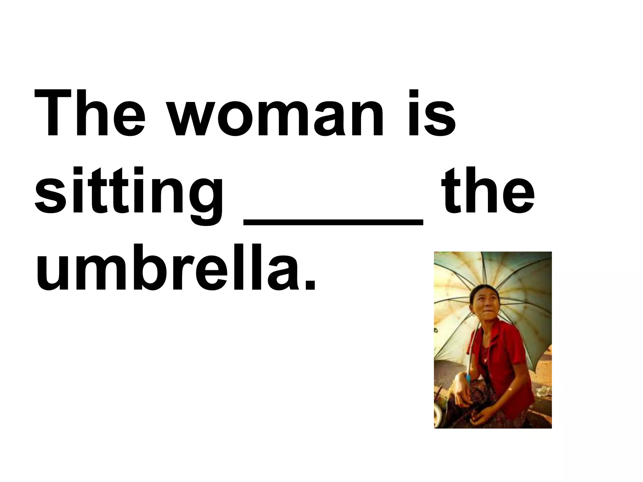 The woman is sitting _____ the umbrella.