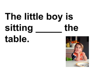 The little boy is sitting _____ the table.