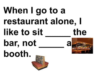 When I go to a restaurant alone, I like to sit _____ the bar, not _____ a booth.