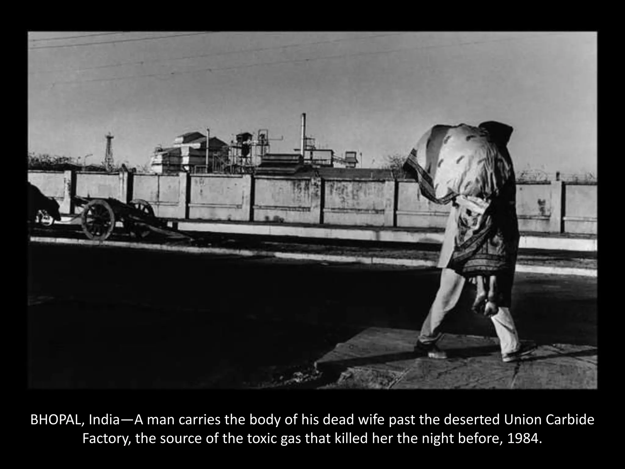 BHOPAL, India—A man carries the body of his dead wife past the deserted Union Carbide Factory, the source of the toxic gas that killed her the night before, 1984.