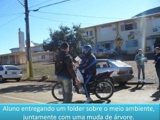 Aluno entregando um folder sobre o meio ambiente, juntamente com uma muda de árvore.