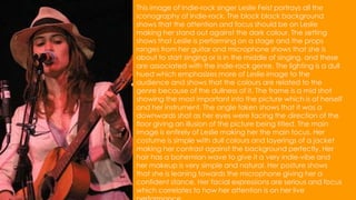This image of Indie-rock singer Leslie Feist portrays all the
iconography of Indie-rock. The block black background
shows that the attention and focus should be on Leslie
making her stand out against the dark colour. The setting
shows that Leslie is performing on a stage and the props
ranges from her guitar and microphone shows that she is
about to start singing or is in the middle of singing, and these
are associated with the indie-rock genre. The lighting is a dull
hued which emphasizes more of Leslie image to the
audience and shows that the colours are related to the
genre because of the dullness of it. The frame is a mid shot
showing the most important into the picture which is of herself
and her instrument. The angle taken shows that it was a
downwards shot as her eyes were facing the direction of the
floor giving an illusion of the picture being titled. The main
image is entirely of Leslie making her the main focus. Her
costume is simple with dull colours and layerings of a jacket
making her contrast against the background perfectly. Her
hair has a bohemian wave to give it a very indie-vibe and
her makeup is very simple and natural. Her posture shows
that she is leaning towards the microphone giving her a
confident stance. Her facial expressions are serious and focus
which correlates to how her attention is on her live
 